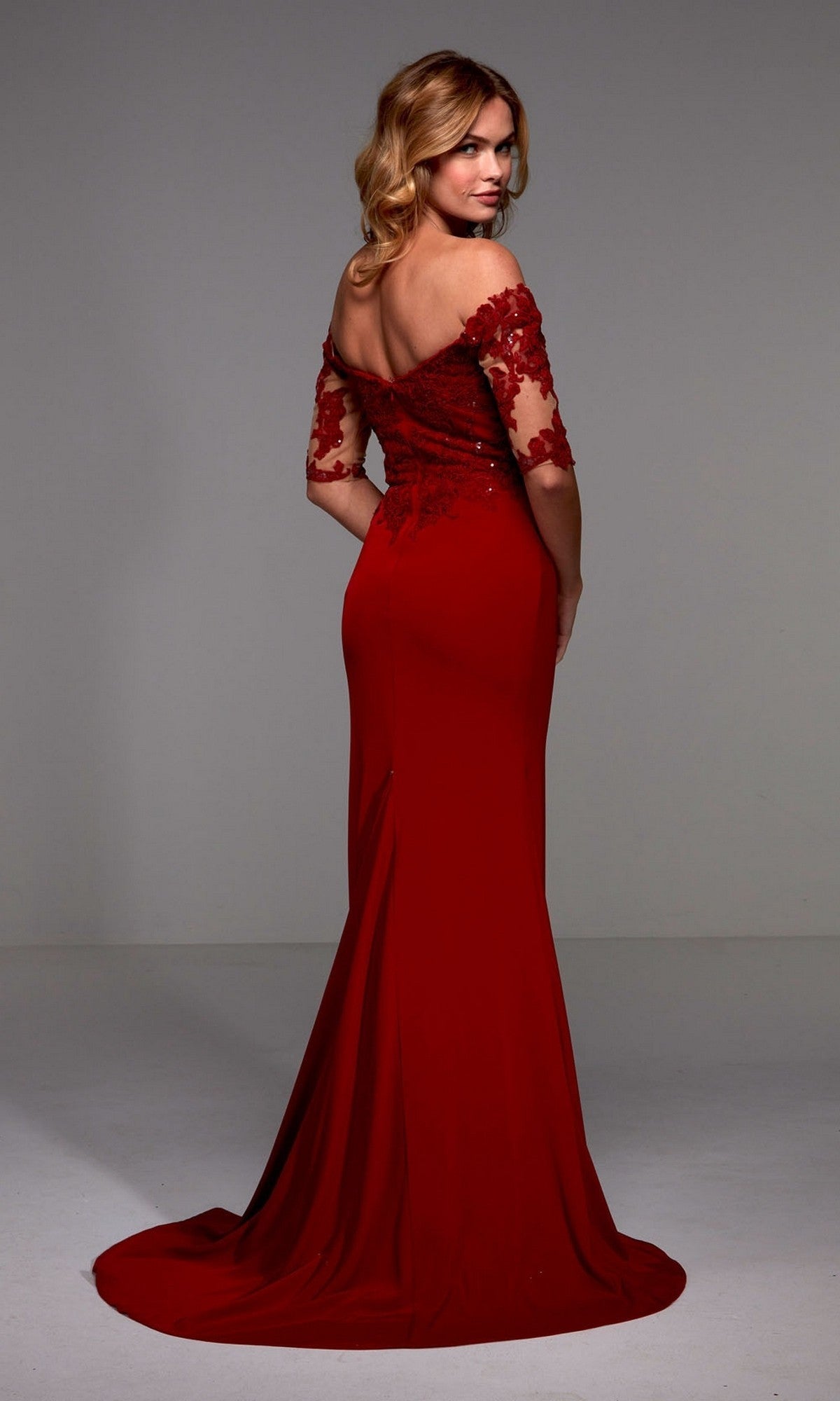 A woman in the Alyce 27518 long formal dress, featuring a red off-the-shoulder sequin lace bodice and sheath crepe floor-length skirt, stands facing backward and looks over her shoulder.